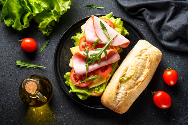 istock Ciabatta sandwich with lettuce, cheese, tomatoes and ham on black table. 2045731213