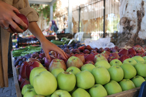 Cropped shot of a young woman picking fresh apples on farmers market. Plant based diet concept. Conscious shopping for organic local produce fruits. Close up, copy space, background.