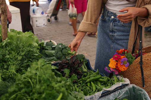 Unrecognizable young woman choosing vegetables, herbs and greens from a stand on farmers market. Shopping for organic local produce. Close up, copy space, background.