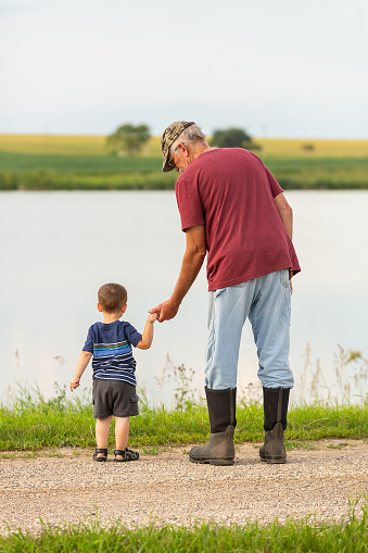 Close-up of a grandfather and young grandson holding hands as they stand on a rural gravel driveway.