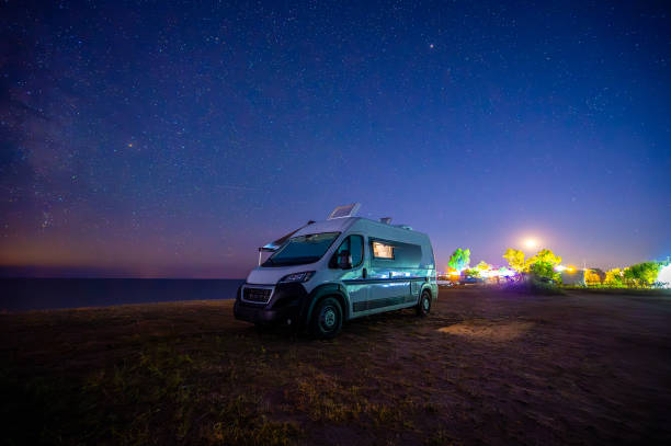 Campervan or motorhome parked on the beach in Greece under the stars and milky way. Tourists enjoying and relaxing on the beach with RV campervan on family vacation.