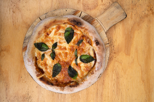 Traditional Margherita pizza. Closeup view of a pizza with mozzarella and parmesan cheese, tomato sauce and basil, on the wooden table.