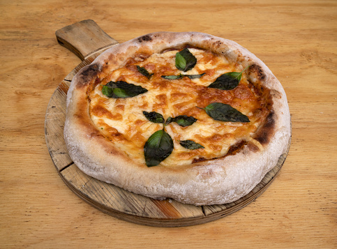 Traditional Margherita pizza. Closeup view of a pizza with mozzarella and parmesan cheese, tomato sauce and basil, on the wooden table.