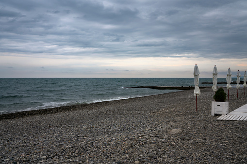 A deserted beach with umbrellas on the Sochi coast against the background of the Black Sea, Adler, Krasnodar Territory, Russia