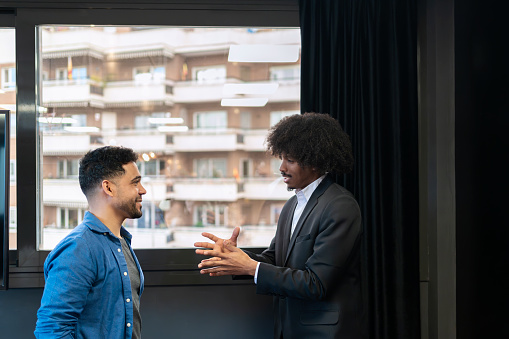 Two professional men in a dynamic discussion with hand gestures, one in casual and the other in formal attire, in an office setting.