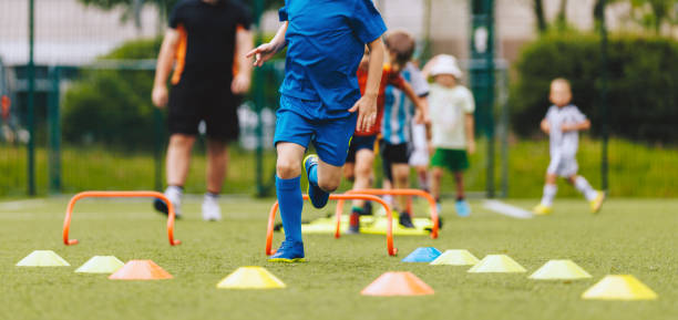 istock Group of children on physical education training with coach. Sport school training for elementary age class. Sporty kids jumping over hurdles on the training field 2045832883