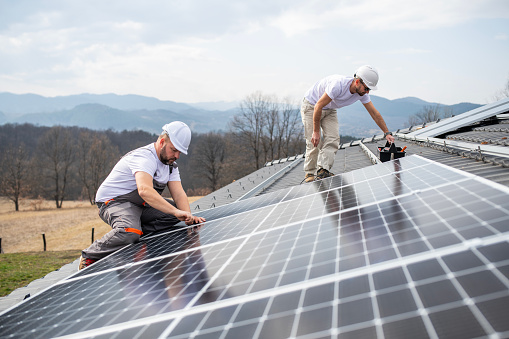 Two workers installing solar panel on roof at new home, Green energy at home, smart home.