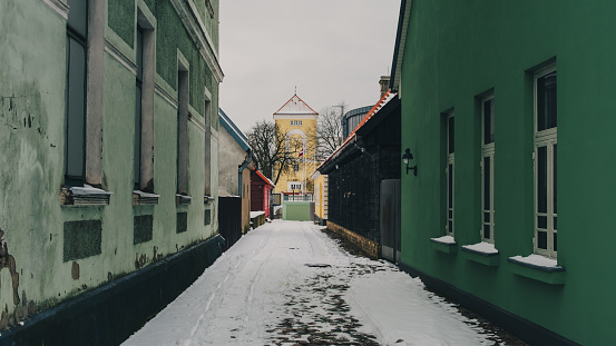 Nestled amidst the quiet charm of Ventspils, Latvija, a narrow street emerges, adorned with a delicate layer of snow, inviting exploration on this serene winter day.