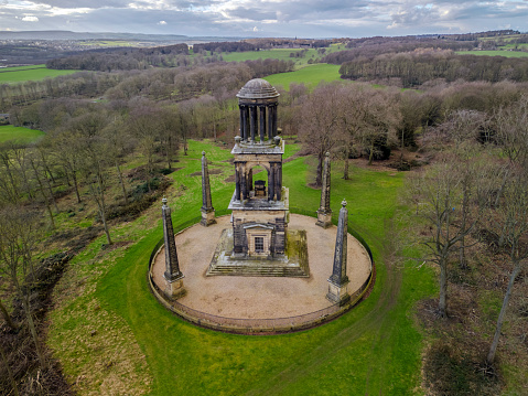 The Rockingham Mausoleum is a Grade I Listed Building in Wentworth Woodhouse Estate, Rotherham, South Yorkshire, England, Feb 2024\n\nThe Rockingham Mausoleum is a Grade I Listed three-storey building 90 ft (27 m) high, situated in woodland, where only the top level is visible over the treetops. It was commissioned in 1783 by the Earl Fitzwilliam as a memorial to the late first Marquess of Rockingham and is just one of several Monuments and Follies in and around Wentworth Woodhouse Estate.\n\nDesigned by John Carr in 1783 as a memorial to the 2nd Marquess. The ground floor contains a statue of the former prime-minister and busts of his eight closest friends by Joseph Nollekens.\n\nThe first floor is an open colonnade with Corinthian columns surrounding an (empty) sarcophagus. The top storey is a Roman-style cupola.