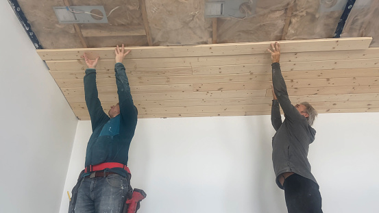 Senior and young man stand on scaffolding and build tongue and groove ceiling together