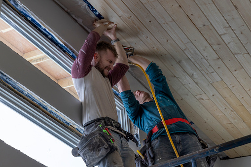 Young men stand on scaffolding and build tongue and groove ceiling together