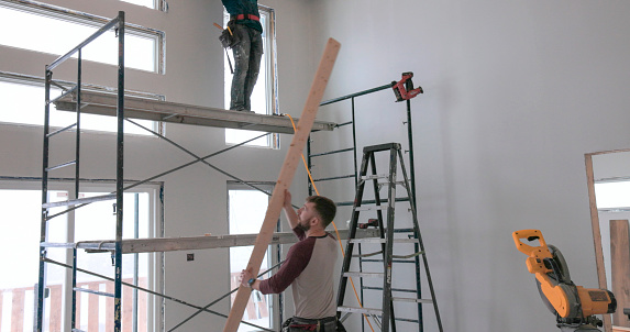 Young men stand on scaffolding and build tongue and groove ceiling together