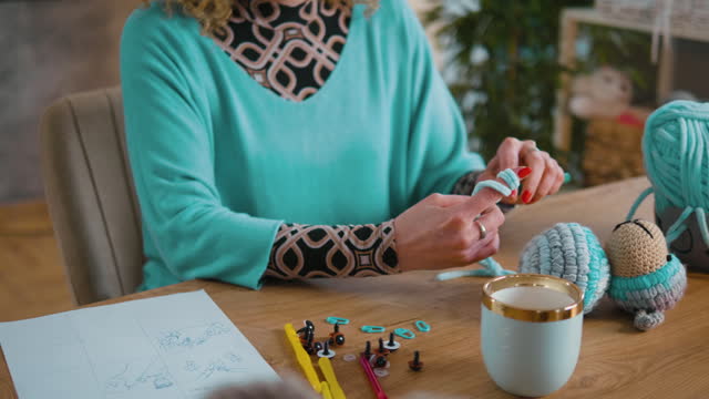 The hands of an unrecognizable woman crocheting at her desk, making stuffed toys