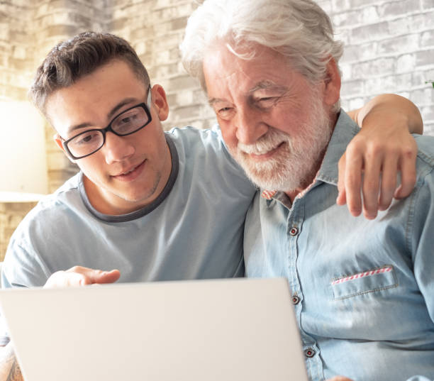 istock Smiling experienced young boy with laptop teaching and showing new computer technology to his old grandfather for surfing internet, shopping online, managing bank. Old man learns to use the computer 2045913970
