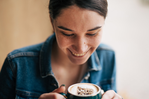 A picture of a young woman sitting in a coffee bar enjoying her coffee. Close up picture.