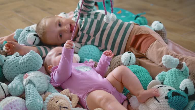 Happy baby at the age of three months lies among stuffed toys and plays with his older brother