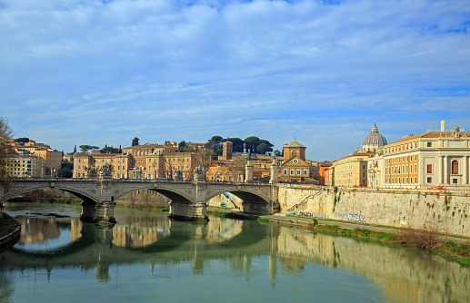 Scenic view over the River Tiber with reflection of arched bridge in calm river and Vatican Basilica in the distance, Rome, Italy