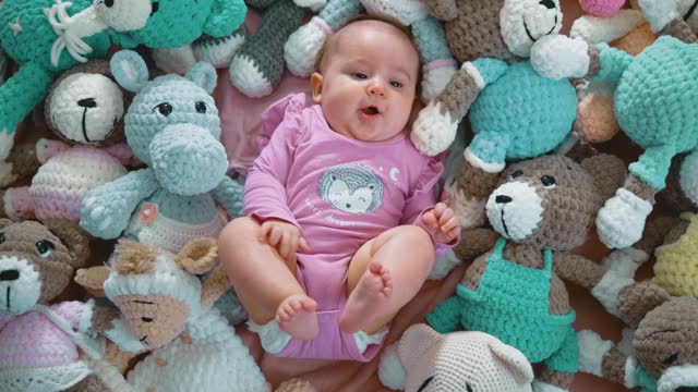Portrait of a small cute newborn baby lying between knitted stuffed toys