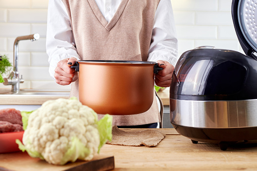 Woman hand using modern multi cooker in a kitchen. Female hand hold pot or products. Preparation for cooking with crockpot.