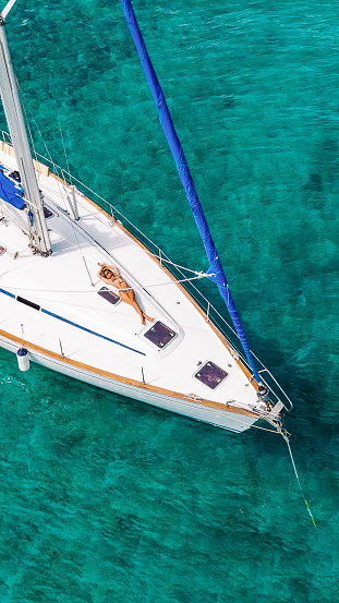 Gorgeous young woman lying, sunbathing and enjoying on sailboat anchored in bay with beautiful crystal clear water.