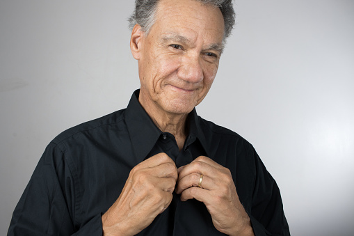 Mature Senior Man buttoning up his shirt while getting dress for work
