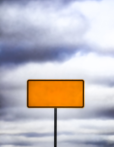 A yellow directional sign against cloudy sky