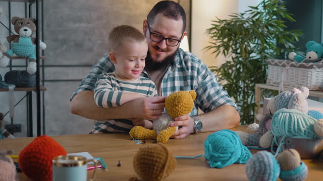 Little happy boy playing making knitted toys with dad at home in  workshop at desk. The concept of a small family business