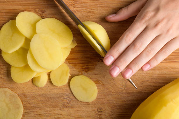 istock Authentic female hands cutting potatoes on wooden cutting board on gray kitchen table 2046005390