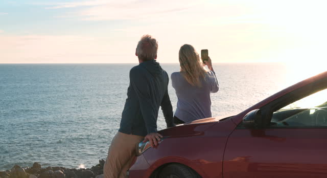 Mature couple look off to sea from parked vehicle