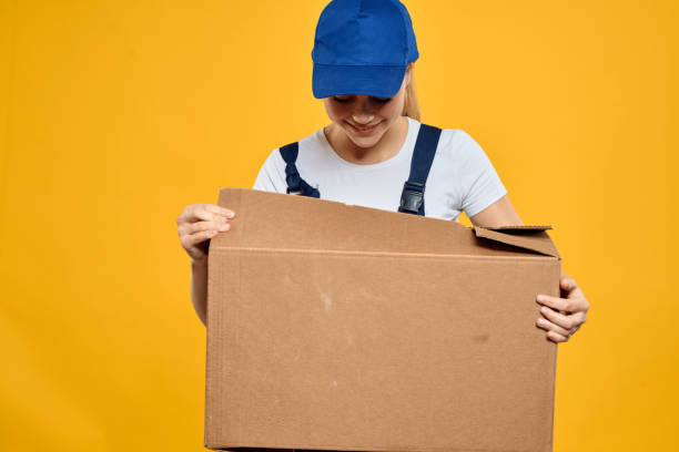 istock Working woman in uniform box in hands delivery courier service rendering yellow background 2046011249