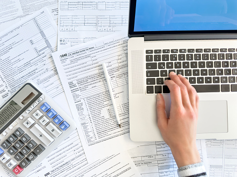 Close up photo of a woman doing taxes with laptop and tax forms in a house