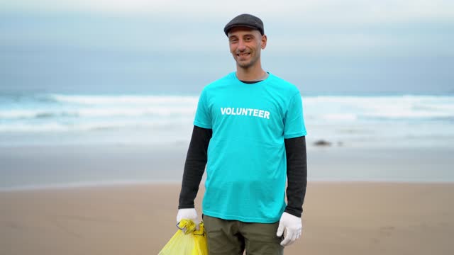 volunteer holding plastic bag full of rubbish cleaning a beach