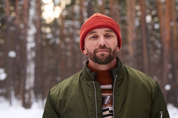Portrait of young Caucasian man wearing warm clothes standing in forest on winter day
