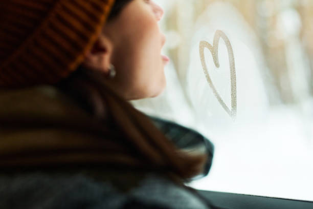 Closeup of romantic young woman drawing heart on frosty car window