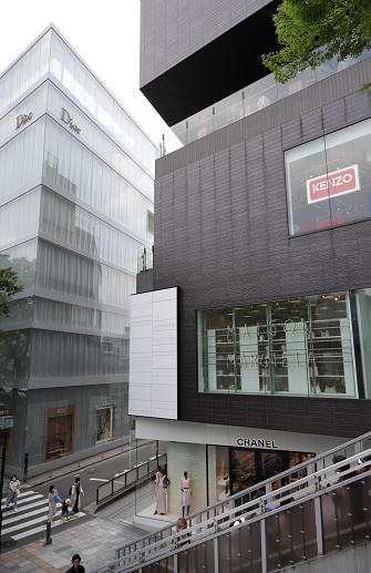 Shibuya, Japan - May 22, 2023: Pedestrians walk outside prominent stores in upscale Omotesando. View from the pedestrian walkway above Route 413 in the Jingumae District. Spring morning with hazy skies above the Tokyo Metropolis.