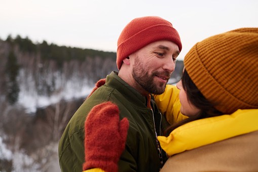 Medium closeup of bearded Caucasian man hugging his wife while standing outdoors on winter day