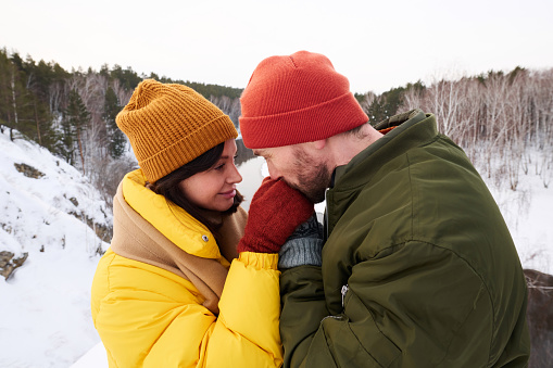 Side view shot of Caucasian couple having date in mountains on winter day, man kissing his girlfriends hand