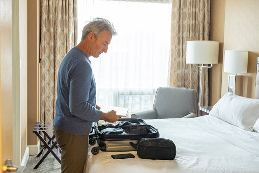 Mature man organizes suitcase on bed in hotel room