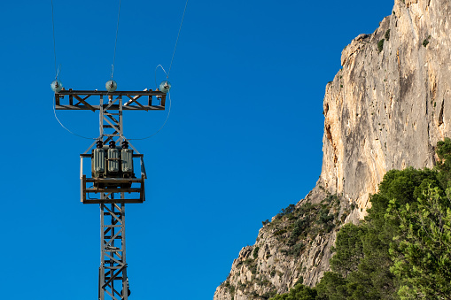 A pole with high voltage electrical wires against a background of blue sky and Mountain in the Alicante region of Spain in summer, Cordillera.