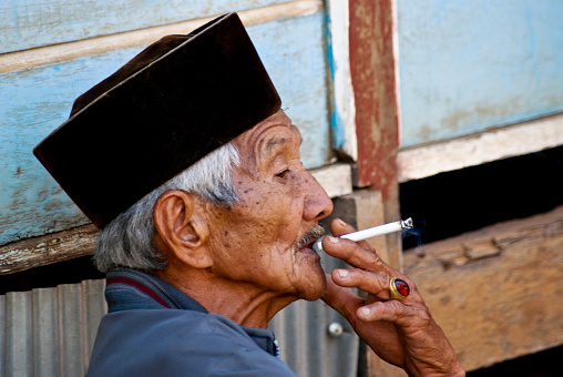Tana Toraja, Sulawesi, Indonesia - Oct 20, 2009: portrait of elderly man smoking while watching the passing of a funeral procession during a traditional Toraja funeral