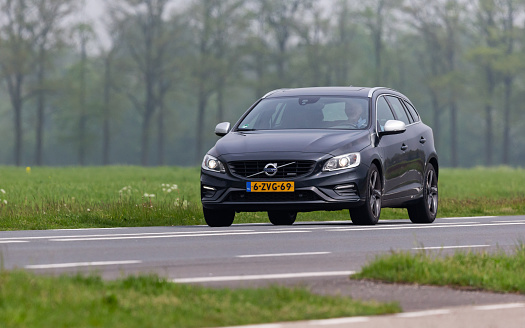 Netherlands, Overijssel, Twente, Hengelo, Oele, May 9th 2023, side/front view close-up of a man driving in a gray 2015 hybrid Volvo 1st generation V60 station wagon on the N739 at Oele, the V60 has been made by Swedish manufacturer Volvo since 2010, the N739 is a 10 kilometer long highway in Twente