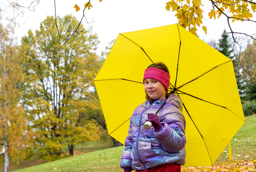 Portrait of a 7-year-old Caucasian girl with a bright yellow umbrella in an autumn park.
