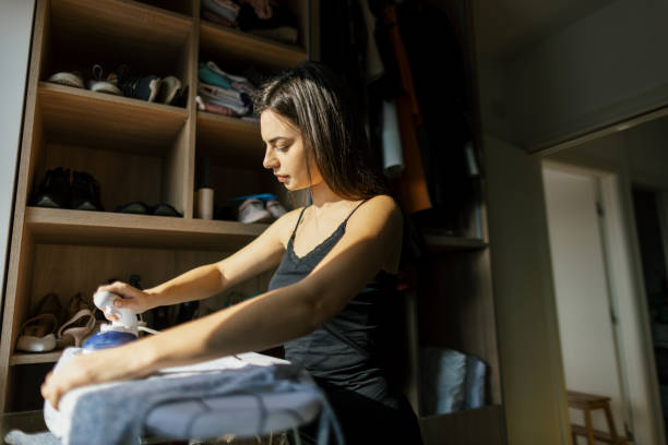 young woman ironing clothes at home - placard women holding standing fotografías e imágenes de stock