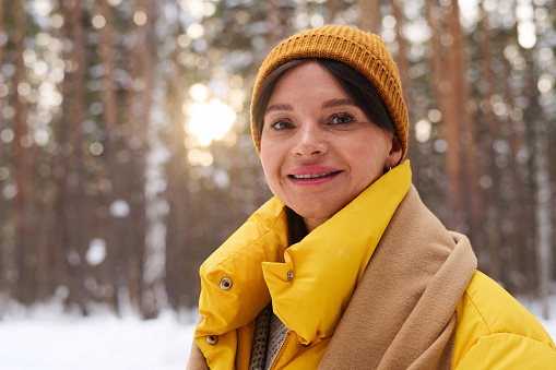 Medium closeup of cheerful Caucasian woman wearing warm clothes standing outdoors on winter day smiling at camera