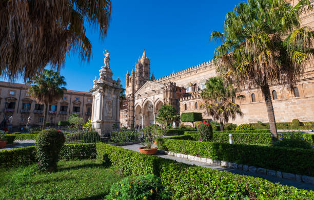 Palermo Cathedral, a magnificent example of Norman architecture, stands proudly in the heart of Palermo, Sicily, Italy, showcasing its intricate design and historical significance. The image depicts a detailed sculpture and gothic architecture of a church behind a manicured ornate garden