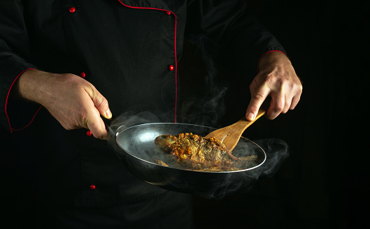 Cooking fried fish in a frying pan in the hands of a chef. Concept of the process of preparing a fish dish in low key with space for advertising.