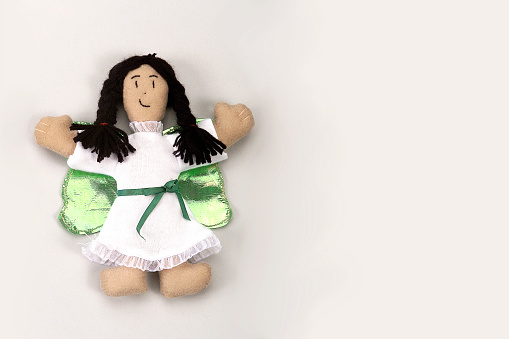 Rag doll, angel with green wings and black braids, isolated on white background, space for text