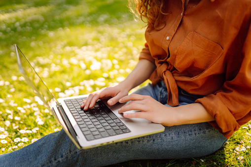 Pretty woman with laptop on the green grass. Education online. IT, Remote work. Business, blogging, freelance concept.