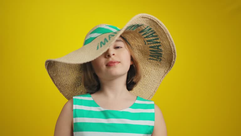 The cute little girl is hiding under the straw hat and smiling cheerfully