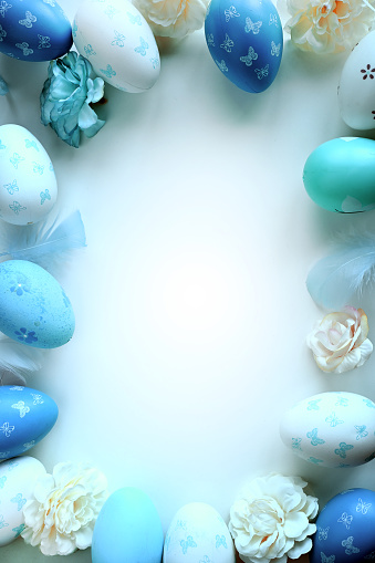 Easter decorations concept. Top view photo of colorful easter eggs, flowers and blue feathers on isolated pastel blue background.
